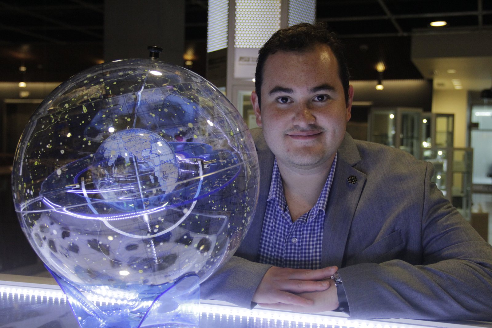 Luis Welbanks seated beside an illuminated transparent celestial globe.